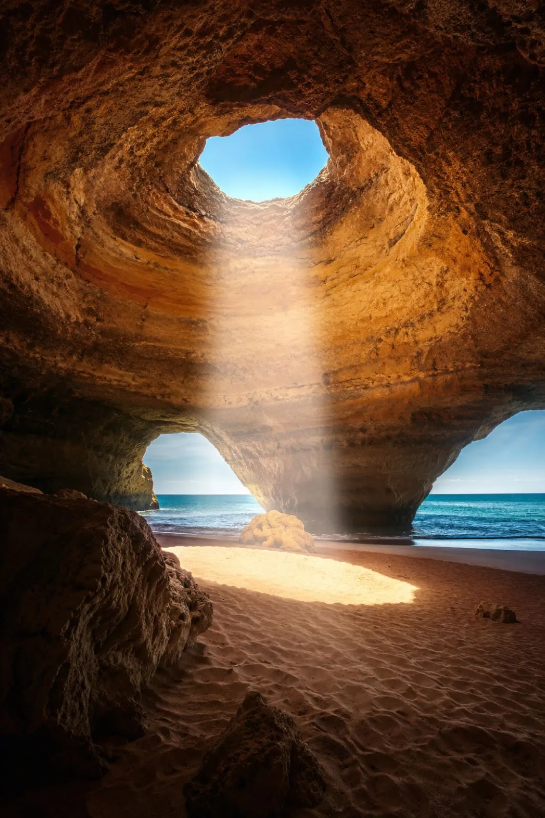 Sunbeam inside Benagil cave opening onto sand